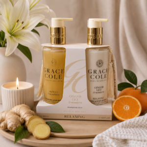 Coffret mains et corps gingembre & mandarine Grace Cole, présenté sur un plateau en bois avec lys blanc, racine de gingembre, mandarines et bougie allumée